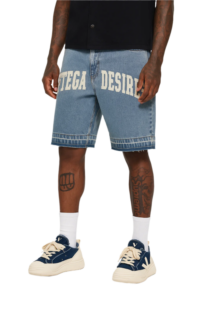 Person wearing blue denim shorts with 'DESIRES' printed on them, paired with navy sneakers and white socks.